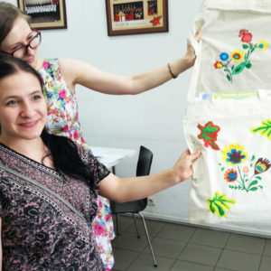 Zdjęcie przedstawia dwie dziewczyny trzymające w rękach torby bawełniane z namalowanymi na nich kolorowymi motywami kultury słowiańskiej wykonane podczas zajęć z kultury i języka słowiańskiego SLAVICA