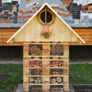 Zdjęcie przedstawia drewniany hotelik dla owadów znajdujący się przed budynkiem TCK