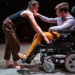 Kadr ze spektaklu "Koszt życia" przedstawia kobietę pochylającą się nad mężczyzną siedzącym na wózku inwalidzkim