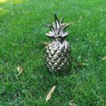 Zdjęcie przedstawia figurę srebrnego ananasa ustawioną na trawniku