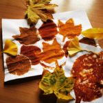 Zdjęcie przedstawia jesienne liście ułożone na leżącej na stole kartce papieru, na której znajdują się kształty liści z przypraw