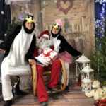 zdjęcie dwóch kobiet przebranych za pingwiny oraz Świętym Mikołajem siedzącym między nimi z napisem #tckonline