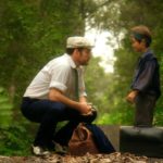 Kadr z filmu na którym kucający mężczyzna rozmawia z małym dzieckiem w środku lasu