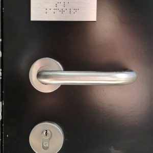 zdjęcie klamki nad która znajduje się tabliczka w języku Braille'a