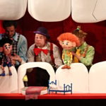 zdjęcie ze spektaklu "Karius i Baktus" aktorzy trzymają lalki teatralne, które siedza wśród scenografii przedstawiającej zęby