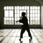 Zdjęcie przedstawia zarys postaci ubranej w strój do azjatyckich sztuk walki na sali gimnastycznej