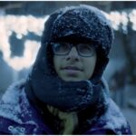 na zdjęciu chłopak w okularach w zimowej czapce i kurtce, które przysypane śniegiem, w tle dużo śniegu