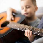 Zdjęcie przedstawia chłopczyka i gitarę